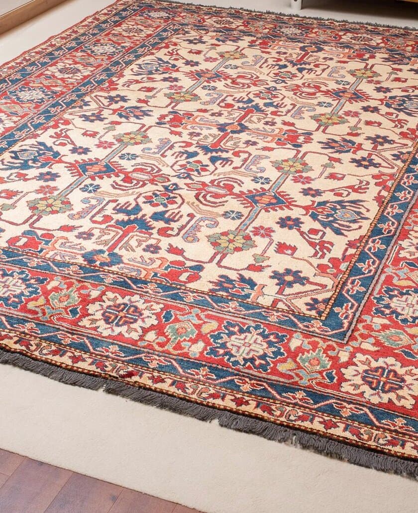 Ausgelegter Teppich mit hellem Feld, rot-blauen Ranken und breiter rot-blauer Bordüre auf hellem Boden